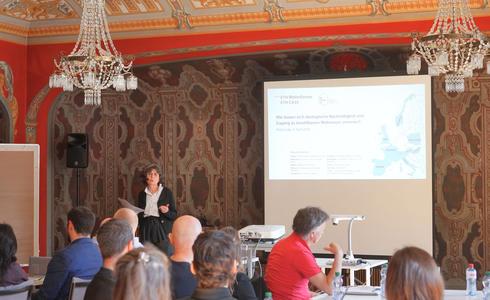 A woman presenting to an audience, in a beautiful historically furnished room
